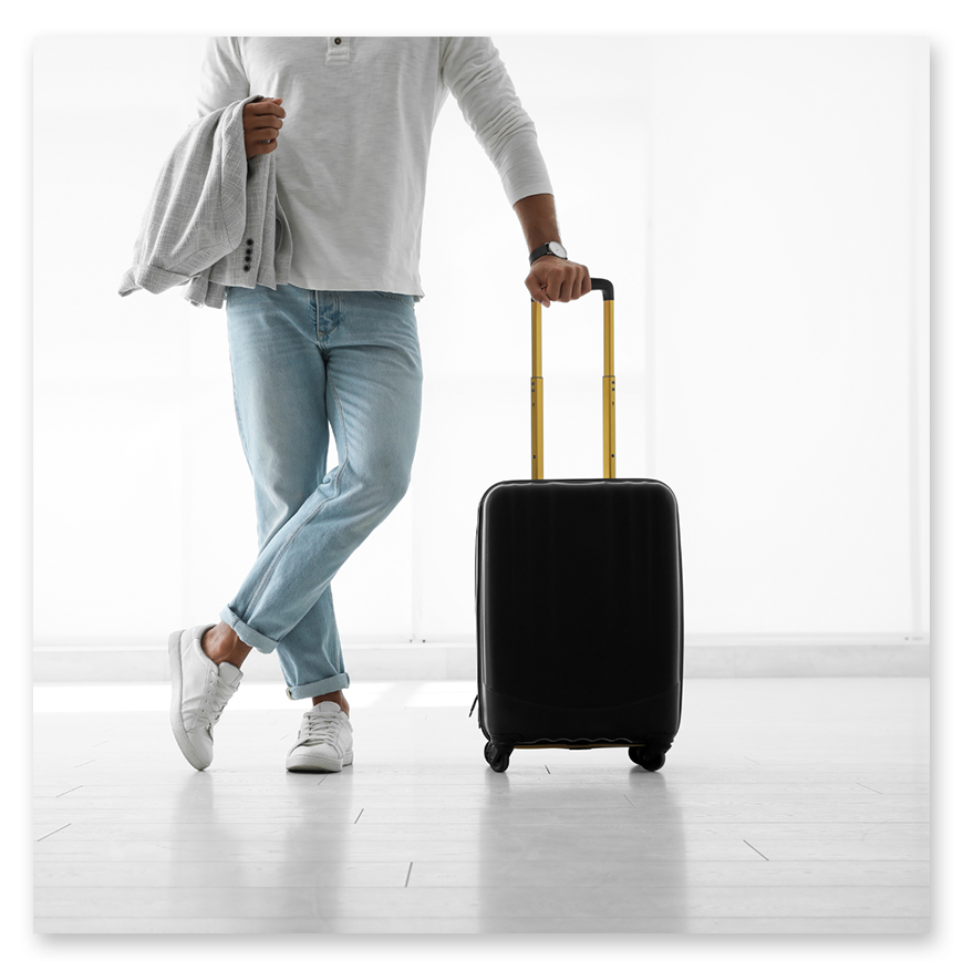 A person stands with a black suitcase, holding a jacket, in a bright, minimalistic setting.